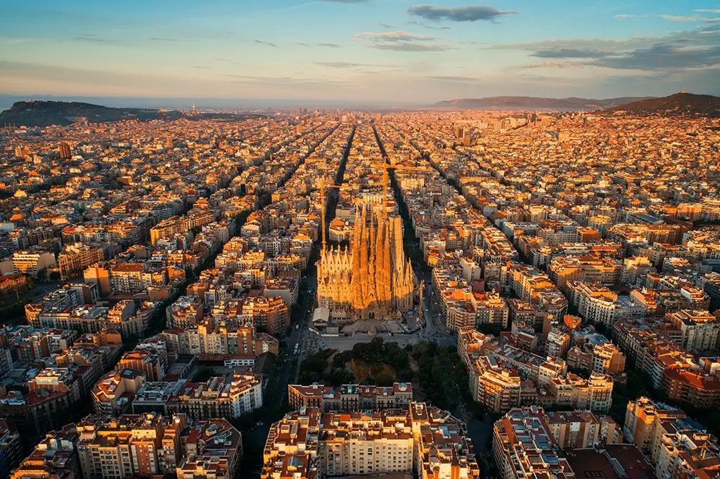Luftaufnahme der Sagrada Fam&iacute;lia in Barcelona, Spanien, umgeben von dicht bebauten Stadtvierteln im warmen Licht der untergehenden Sonne.
